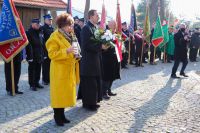 Ksiądz proboszcz z delegacją składa kwiaty pod tablicą przy kościele